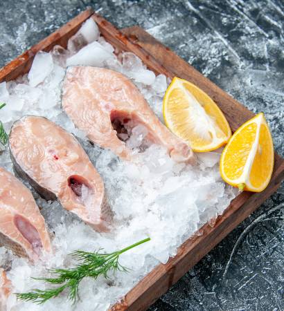 top view raw fish slices with ice lemon slices on wood board on table